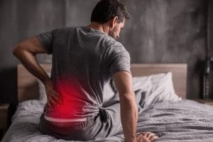 Homem sentado na cama com destaque na região lombar dolorida.