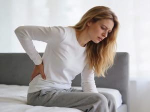 Mulher sentada na cama com dor na região lombar.