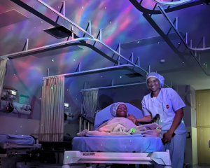 Paciente em ala hospitalar com projeção de céu estrelado e cores roxeadas.