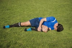 Jogador deitado em campo com dores no joelho