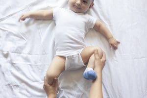 Bebê deitado de barriga para cima com pessoa mexendo em suas pernas