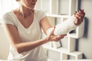Mulher branca segura o braço engessado devido a uma fratura óssea.
