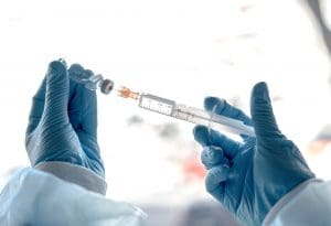 Mãos com luva seguram seringa e uma ampola com remédio.