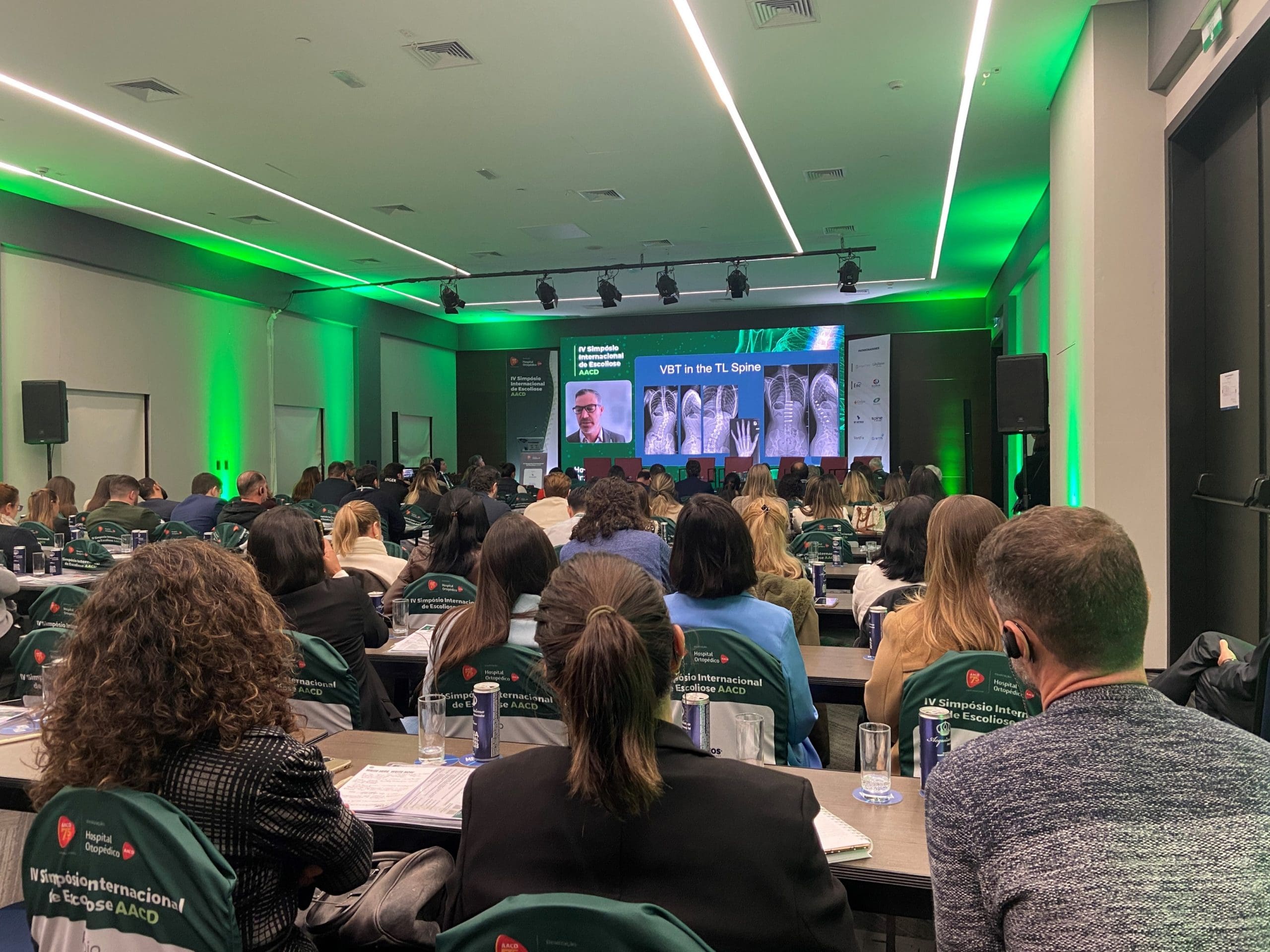 Pessoas sentadas e de costas, prestando atenção em palestra do Simpósio Internacional de Escoliose AACD