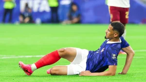 Jogador da França senta no gramado após sentir lesão durante partida.