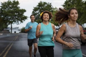 Grupo de adultos pratica corrida em via urbana durante atividade física ao ar livre.