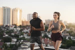 Homem e mulher praticam corrida juntos ao ar livre, com uma paisagem urbana ao fundo.