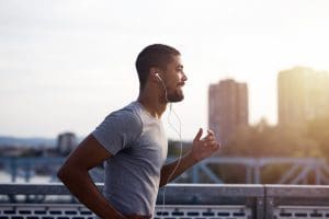 Homem corre ao ar livre utilizando fones de ouvido durante treino de corrida.